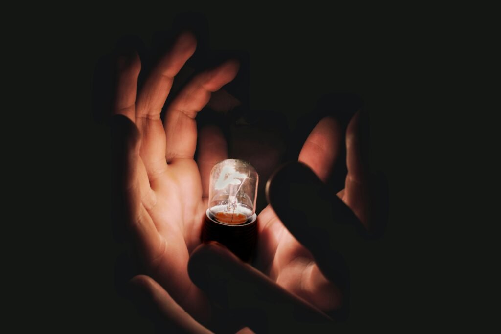 A pair of hands gently cradle a glowing lightbulb, symbolizing energy and innovation.