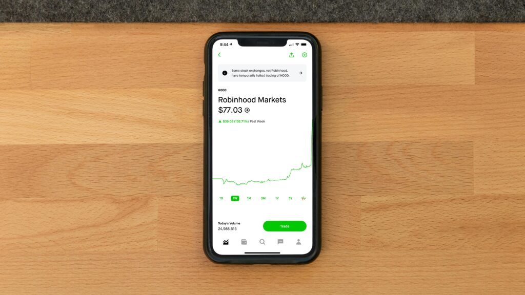 Stock trading app on smartphone displaying Robinhood Markets price on wooden desk.